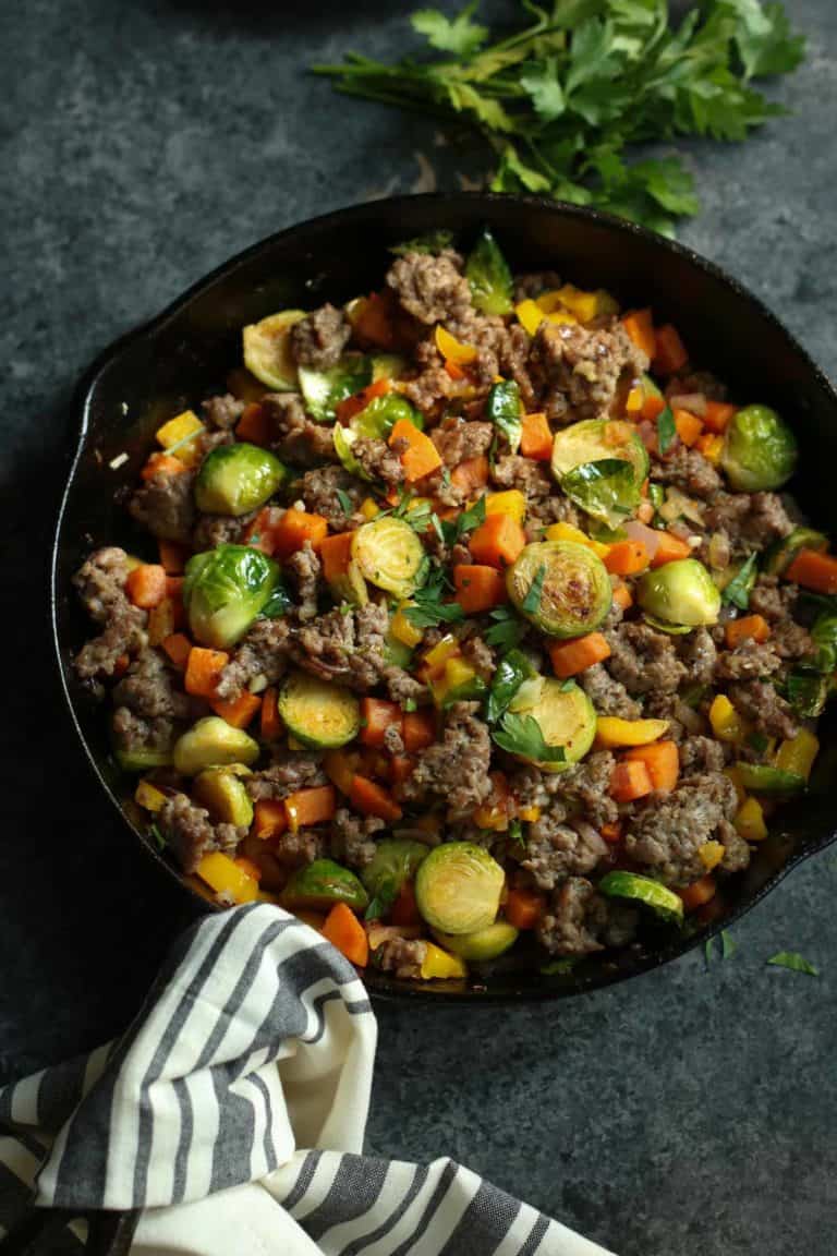Cast iron skillet filled with a breakfast hash featuring sweet potatoes and Brussels sprouts.