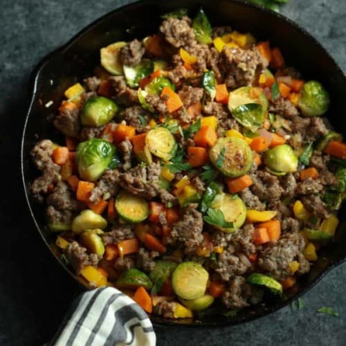 Cast iron skillet filled with a breakfast hash featuring sweet potatoes and Brussels sprouts.