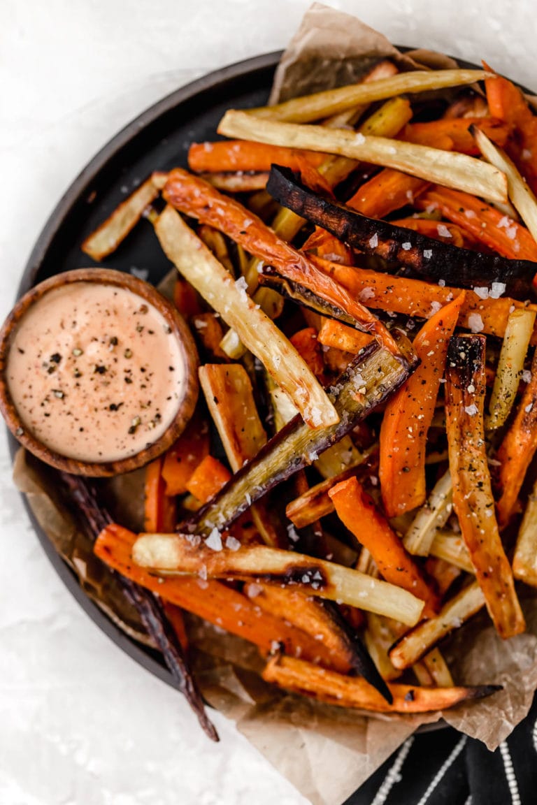 Overhead view of a plate of garlic roasted root vegetable fries with a dipping sauce on the side.