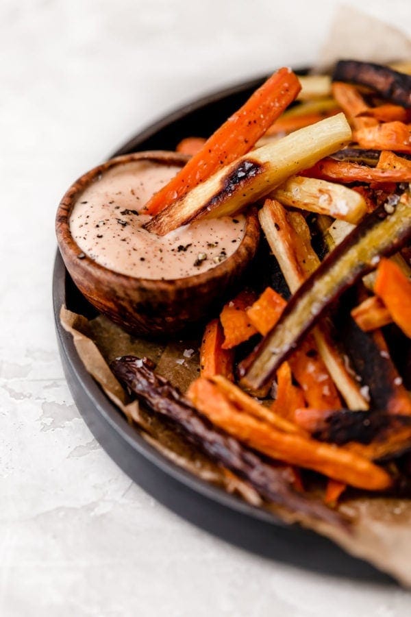 Plate of garlic roasted root vegetable fries with a few shown dipped into a sauce. 