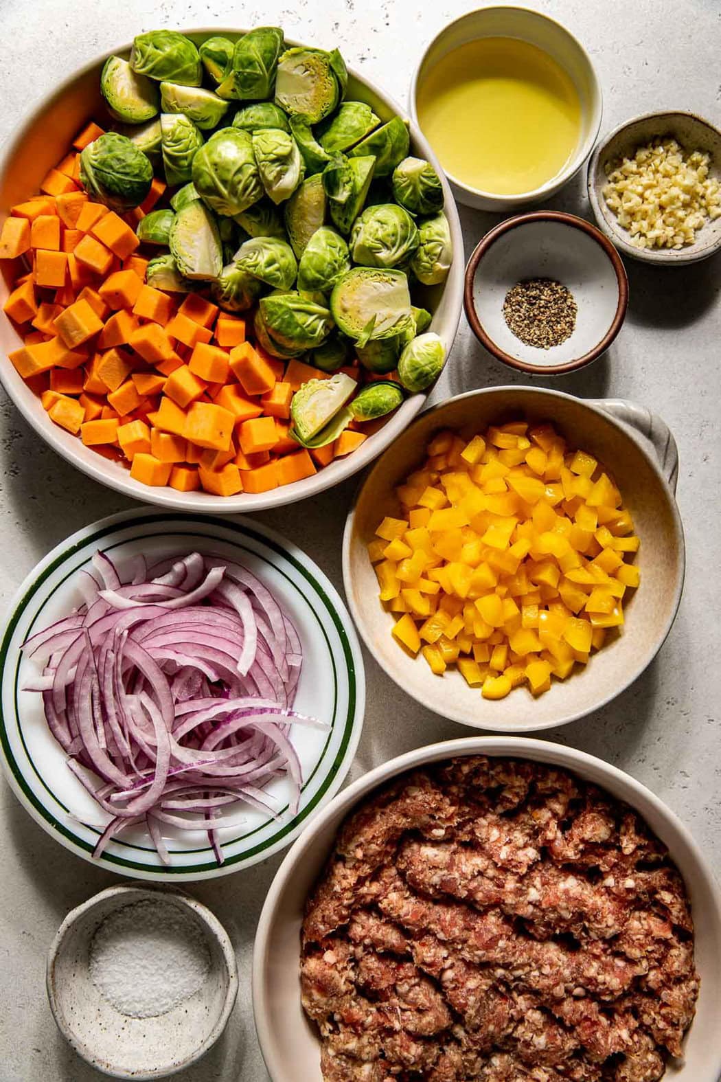 Overhead view of a variety of ingredients for Sweet Potato Hash with Sausage in different sized bowls. 