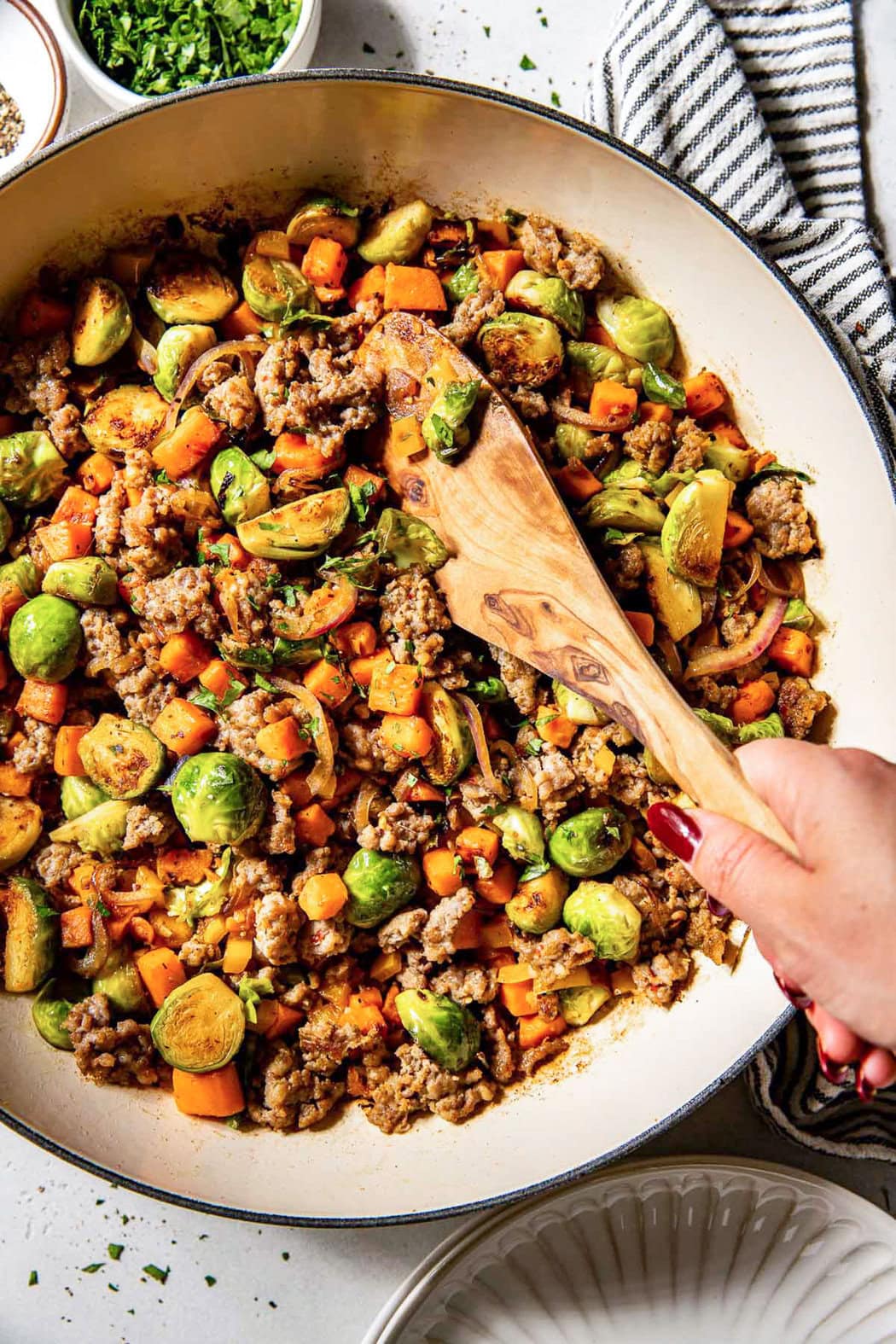 Overhead view of a hand stirring a skillet filled with Sweet Potato Hash with Sausage. 