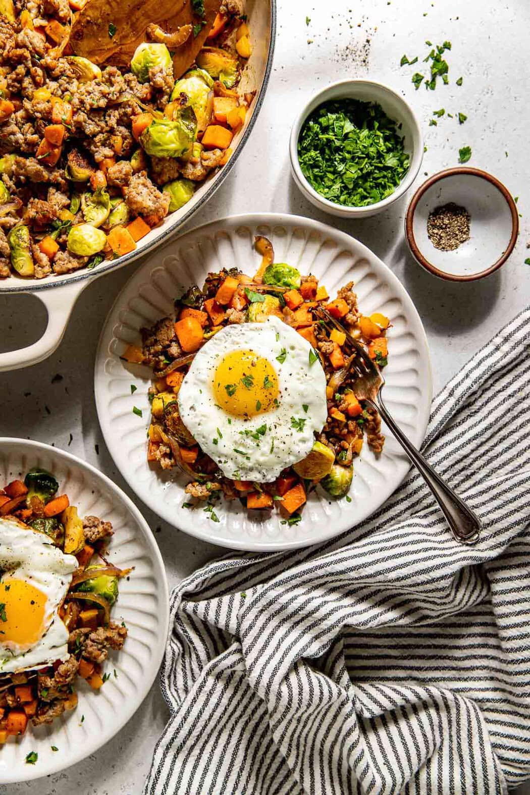 Overhead view of a skillet of freshly sauteed Sweet Potato Hash with Sausage next to a plate topped with a fried egg. 