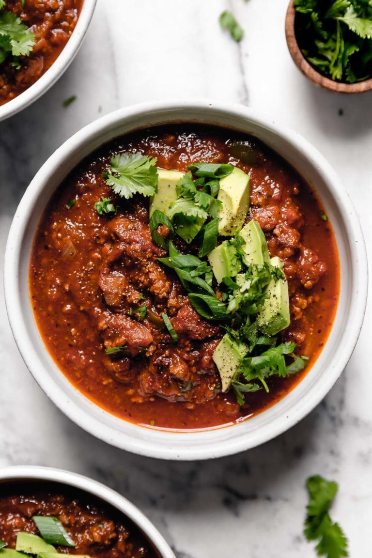 White bowl of slow cooker pumpkin chili topped with green onions and avocado. 