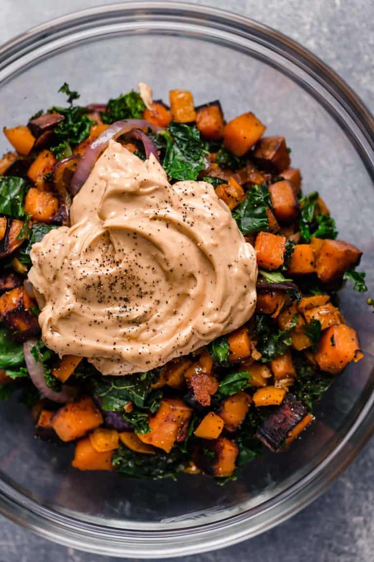 Overhead view of a glass bowl filled with roasted sweet potatoes and topped with a dollop of a chili lime dressing. 