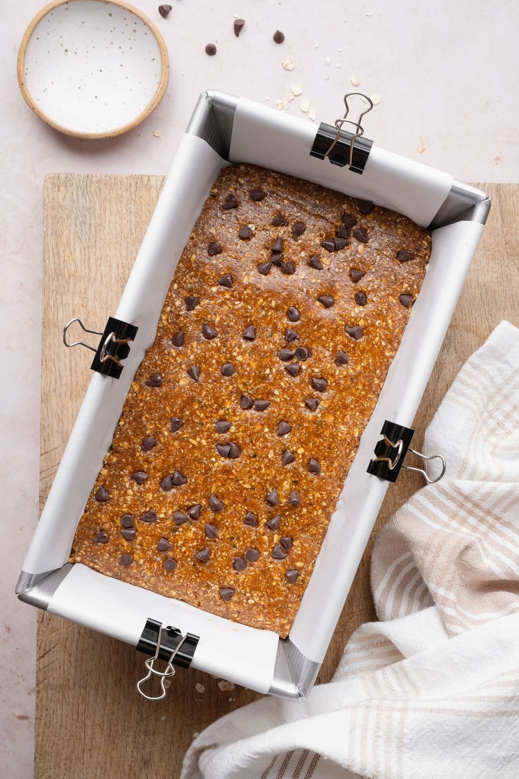 Pumpkin protein bar batter pressed into a parchment-lined loaf pan and topped with chocolate chips.