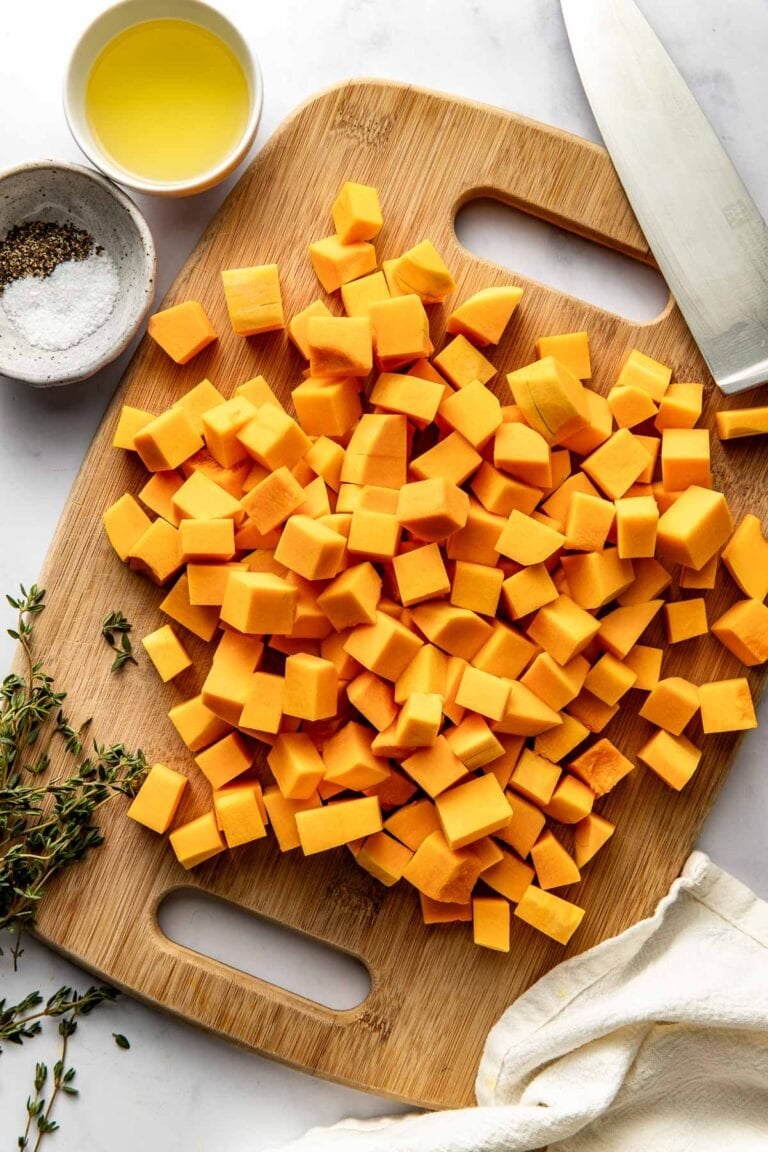 Overhead view of a wooden cutting board filled with cubed butternut squash pieces.
