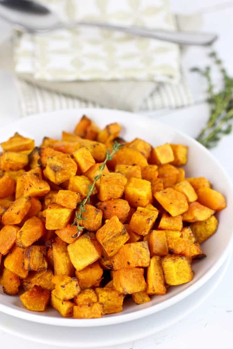 A white plate filled with freshly roasted butternut squash home fries topped with fresh thyme. 