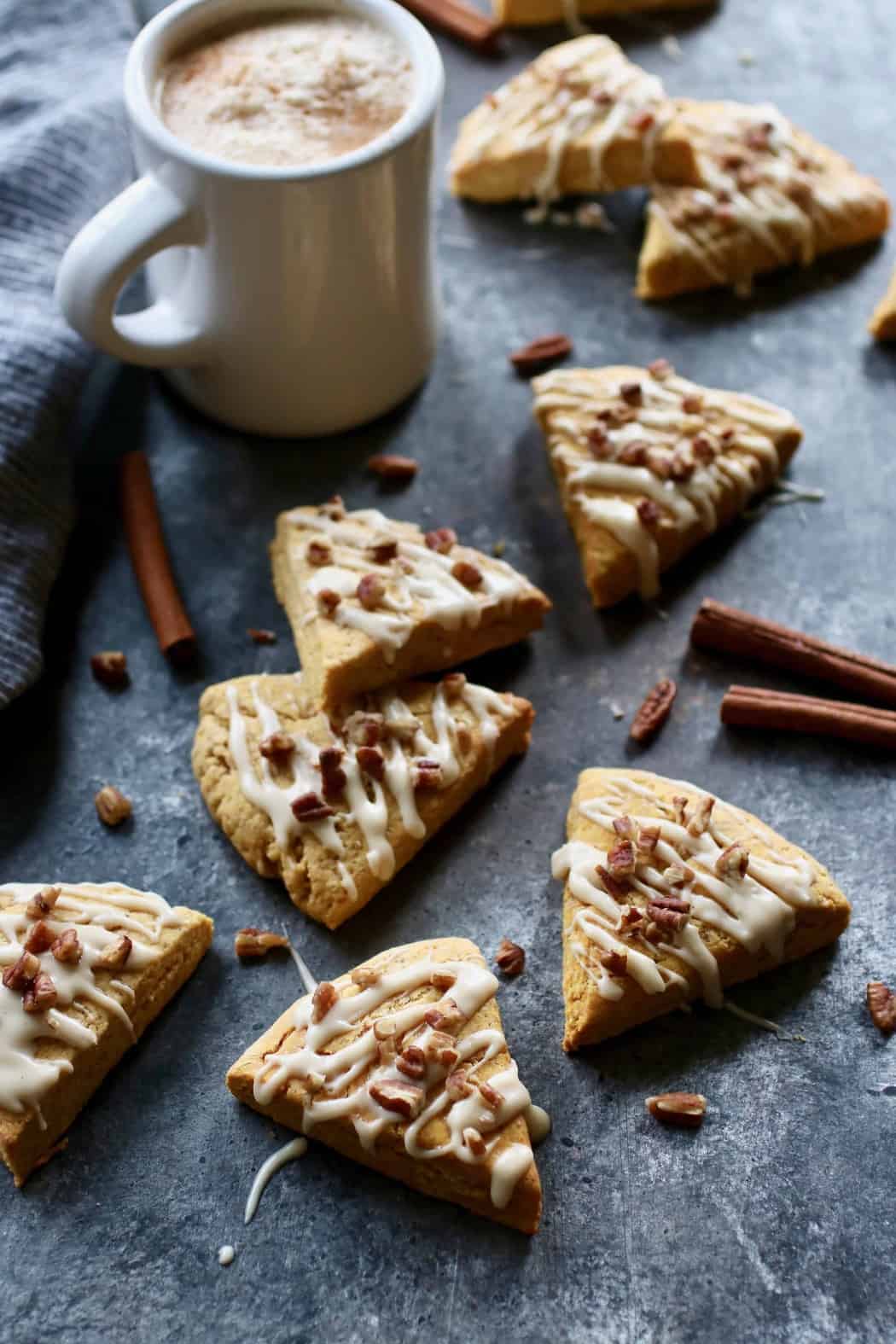 Gluten-free Pumpkin Spice Scones drizzled with frosting scattered about. Cup of coffee in the background.