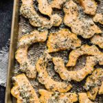 Sheet pan filled with acorn squash slices coated in fresh herbs and Parmesan cheese.
