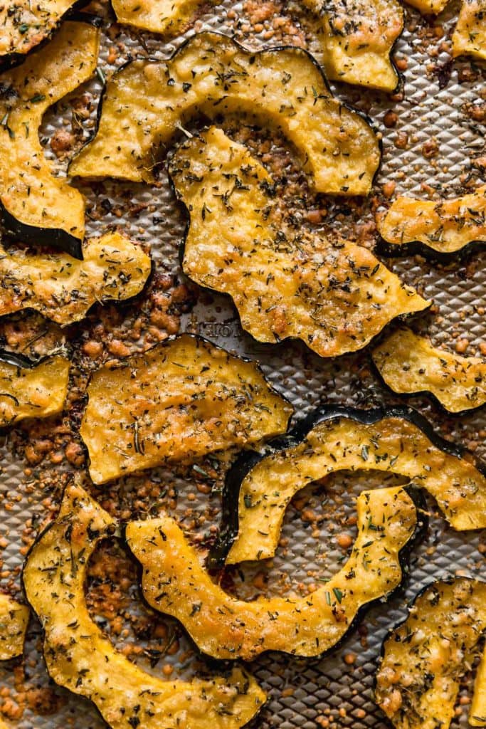 Baking sheet with roasted acorn squash slices coated in fresh herbs and Parmesan cheese.