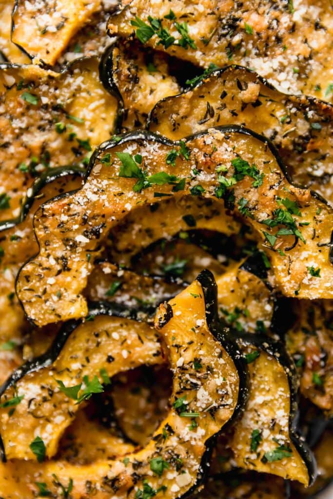 Close up view roasted acorn squash slices with fresh herbs and Parmesan cheese coating each slice.