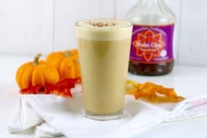 Pumpkin Spice Chai Tea in a tall glass on a white napkin with pumpkins behind it