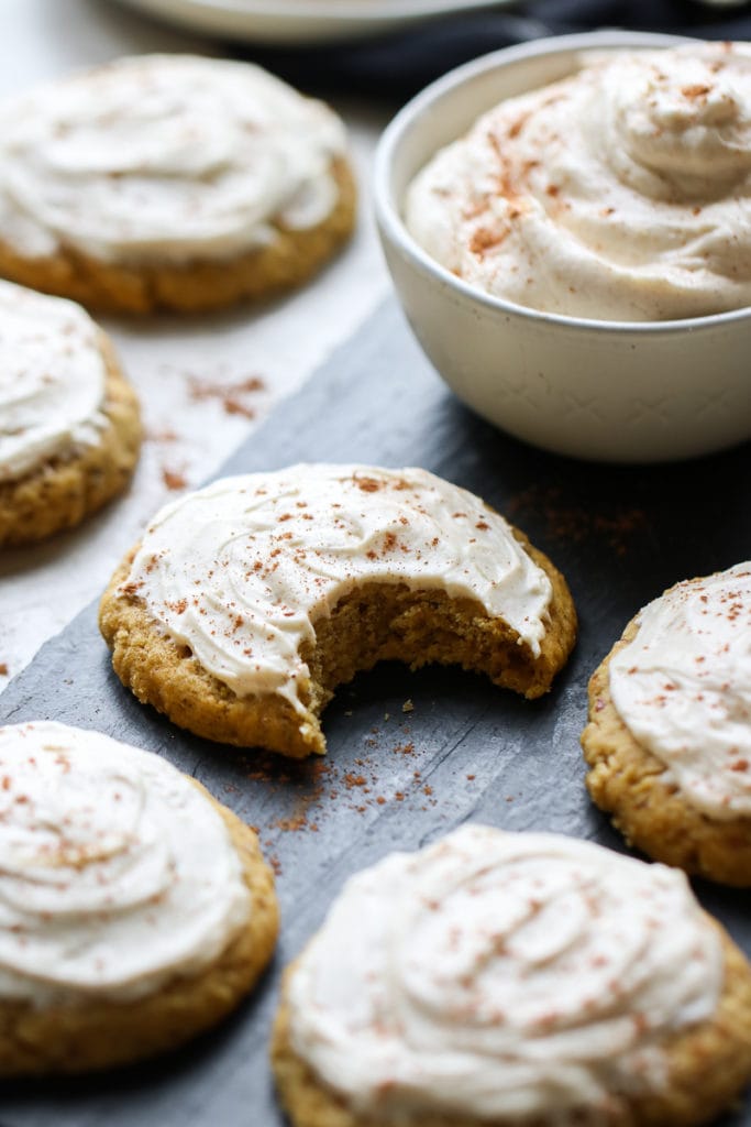 A soft pumpkin cookie with cream cheese frosting in the middle with a large bite taken out of it