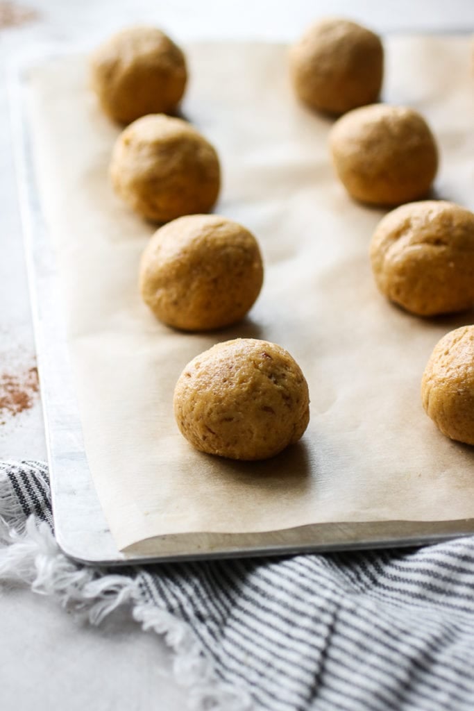 Balled pumpkin cookie dough lined up on a baking sheet on parchment paper