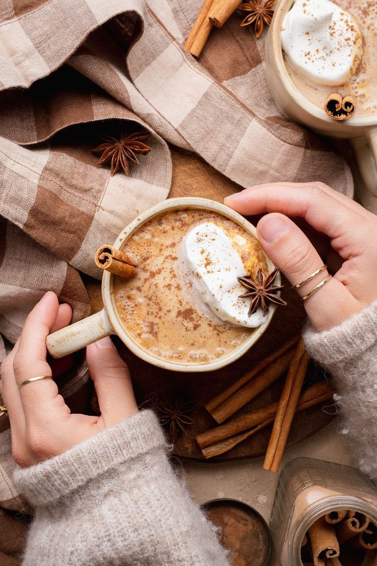 A woman's hand holding a pumpkin chai latte topped with a dollop of whipped cream and star anise.