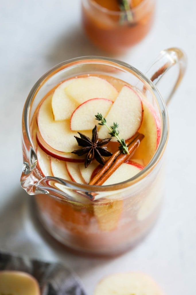 Overhead view of a pitcher filled with apple cider sangria filled with fresh apple and pear slices, cinnamon sticks, fresh thyme, and whole star anise.