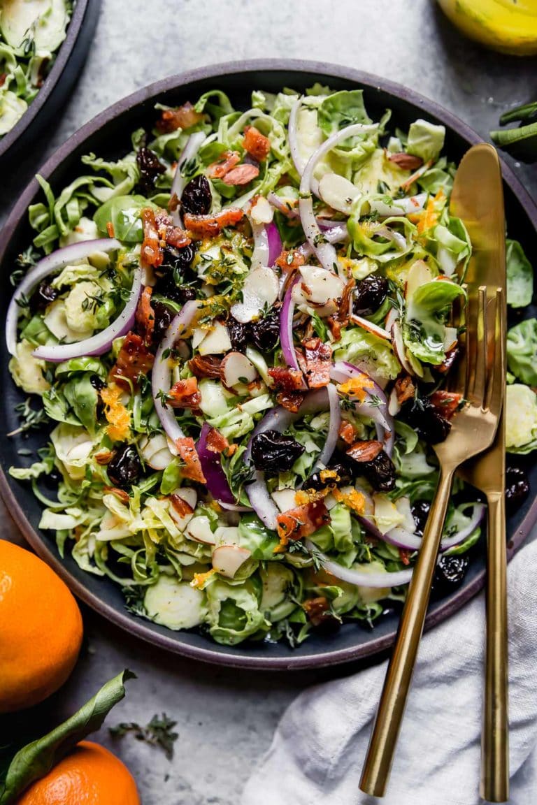 Brussels sprout salad with citrus vinaigrette served in a black bowl topped with bacon and red onion. 