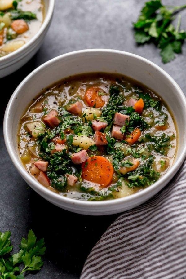 Creamy ham and potato soup with carrots and kale in a cream speckled bowl