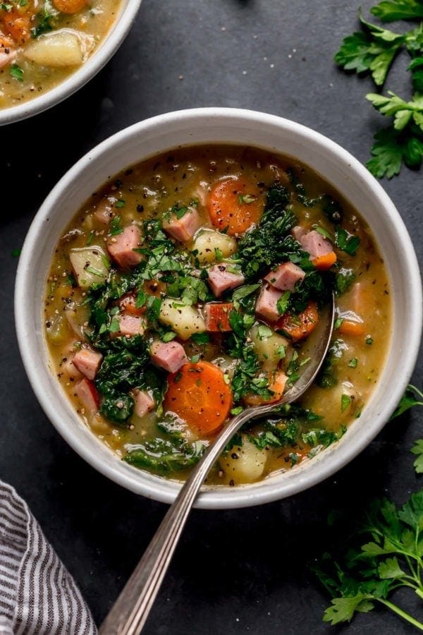 A speckled bowl filled with creamy ham and potato soup topped with kale and herbs