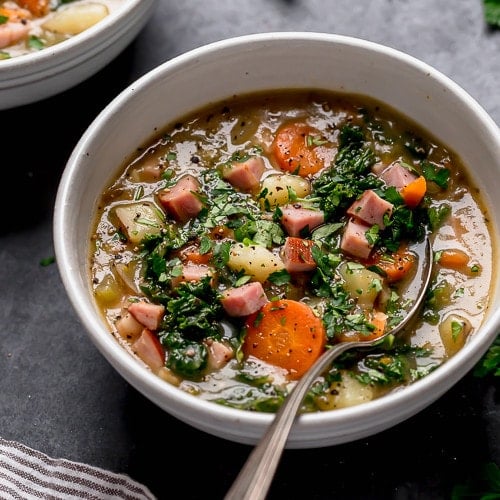creamy ham and potato soup topped with fresh herbs in a speckled bowl