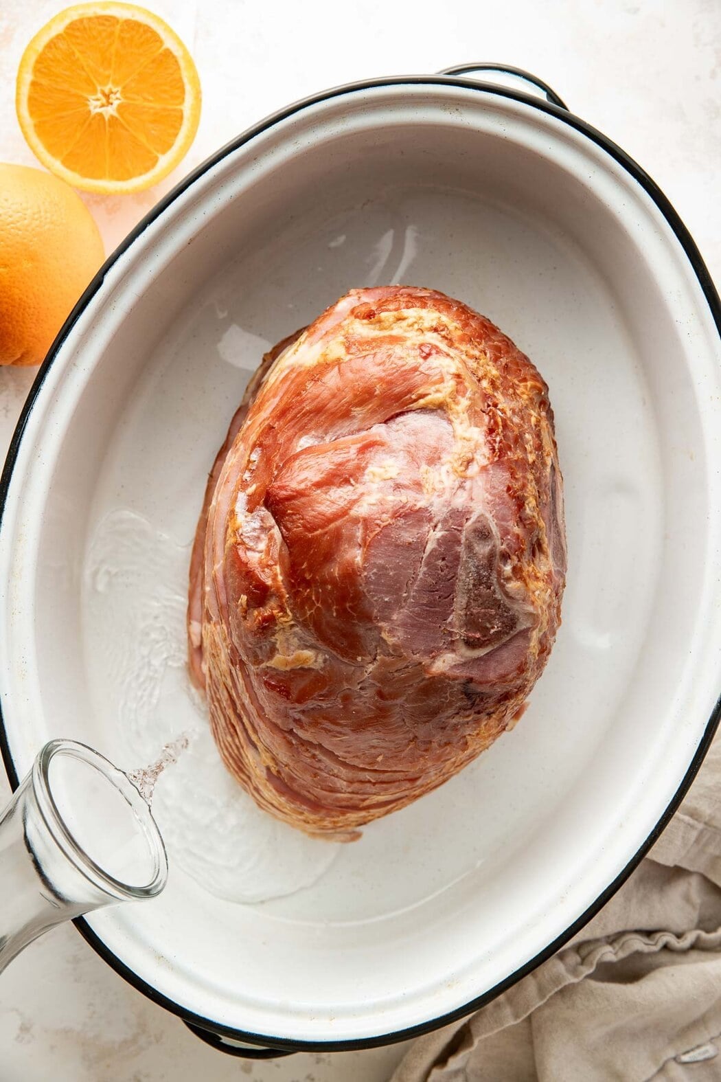 Overhead view of a baking dish filled with a spiral cut ham and water surrounding it.
