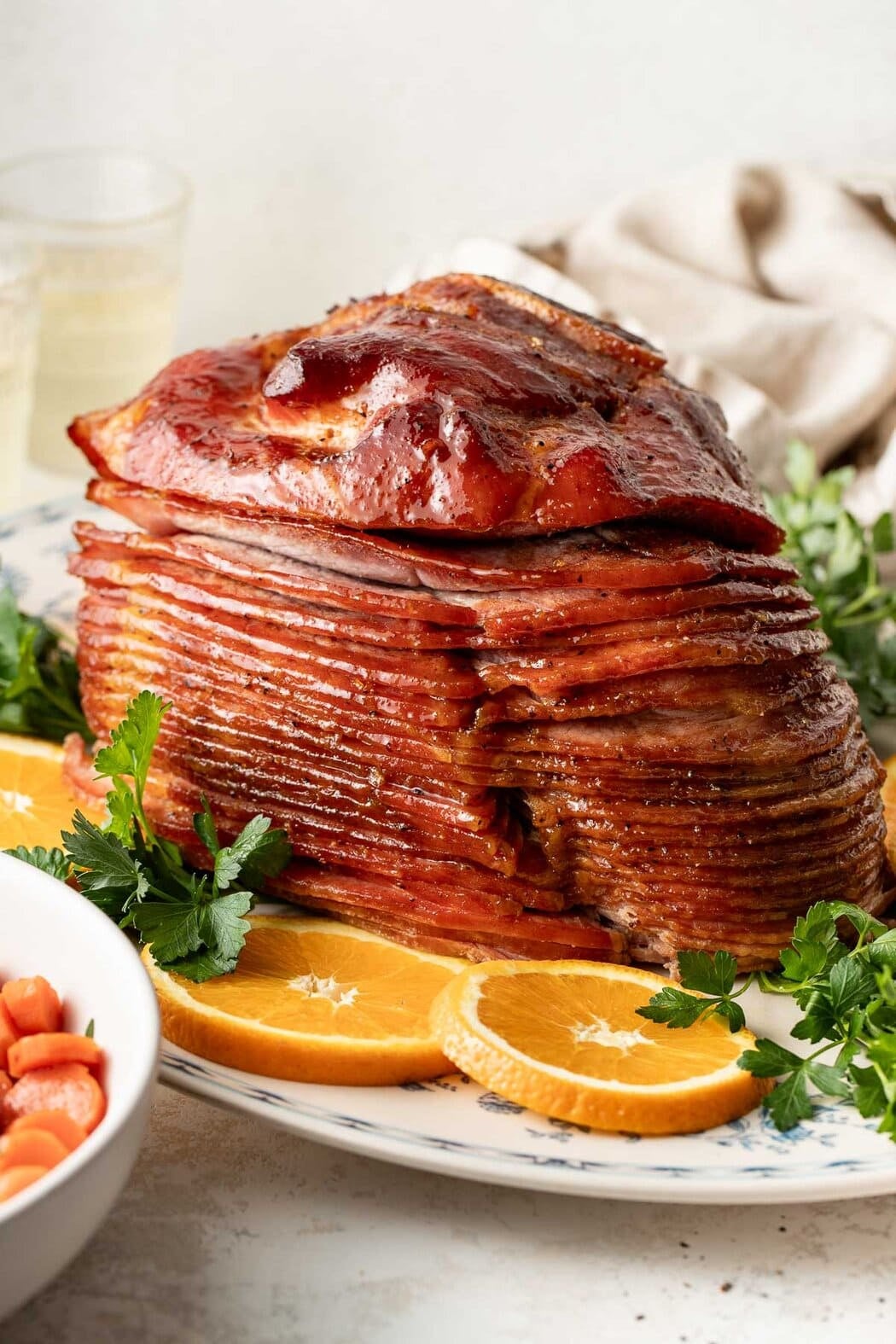 Close up view of a freshly cooked Baked Glazed Ham sliced and surrounded by fresh oranges and herbs.