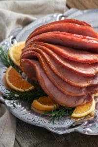 Orange Glazed Ham on a silver platter with sliced oranges resting around it