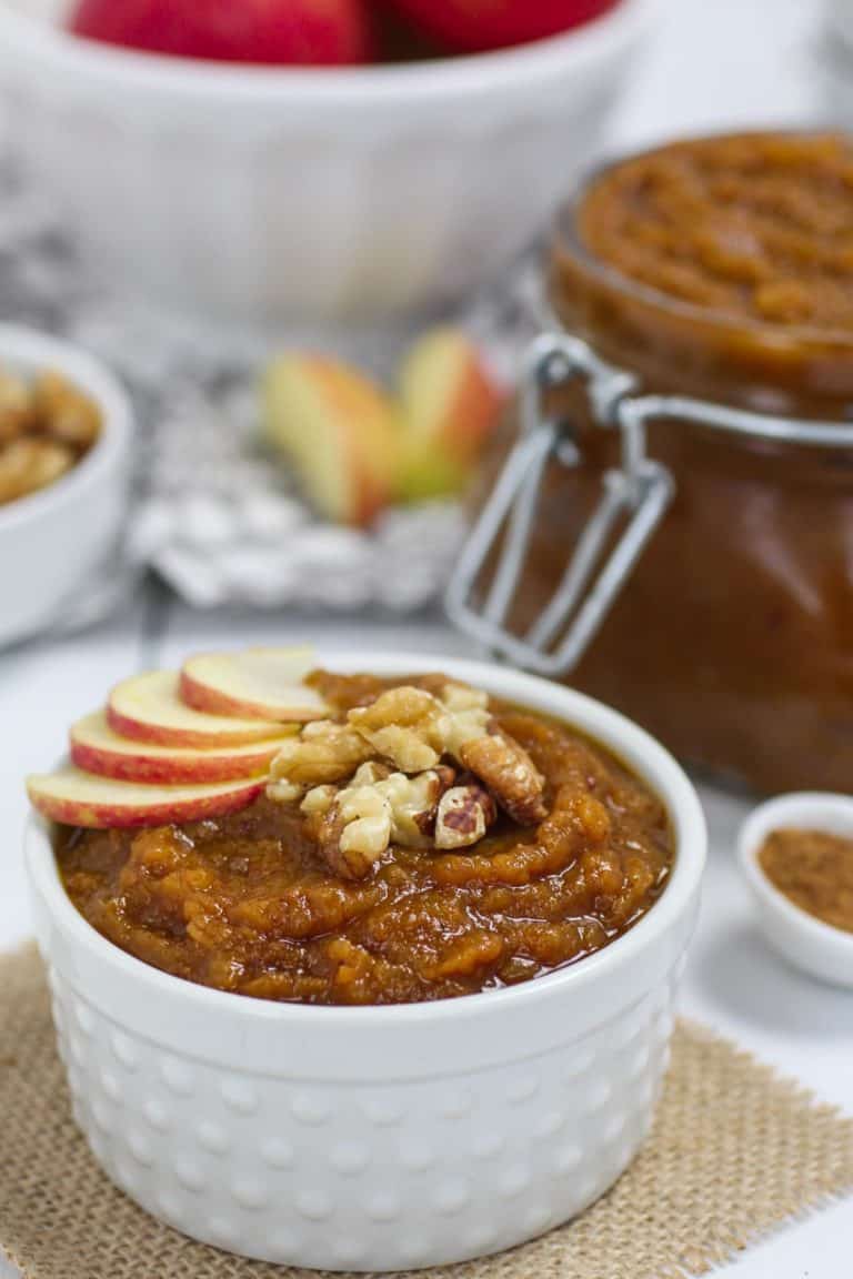 A bowl of slow cooker pumpkin applesauce topped with sliced apples and chopped nuts. 