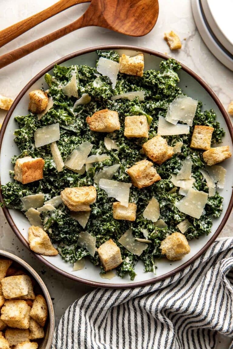 Close up view of a Kale Caesar salad topped with homemade croutons and shaved parmesan cheese. 