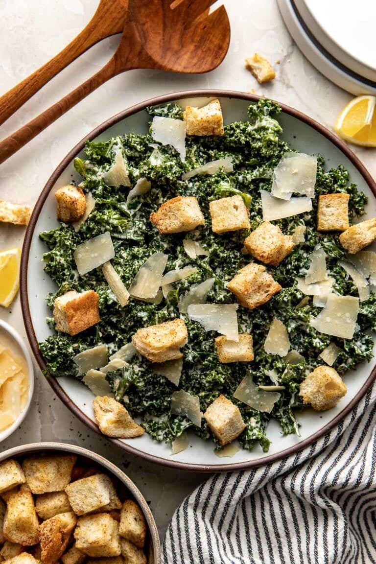 Overhead view of a serving bowl filled with kale Caesar salad topped with shaved parmesan and crunchy croutons. 