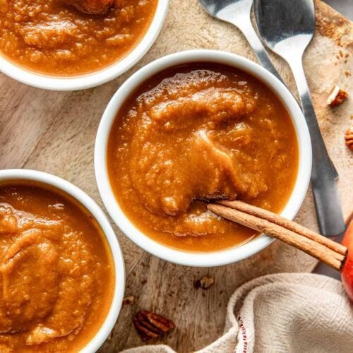 Overhead view of two small bowls of Crockpot Pumpkin Applesauce with a cinnamon stick in the bowl.