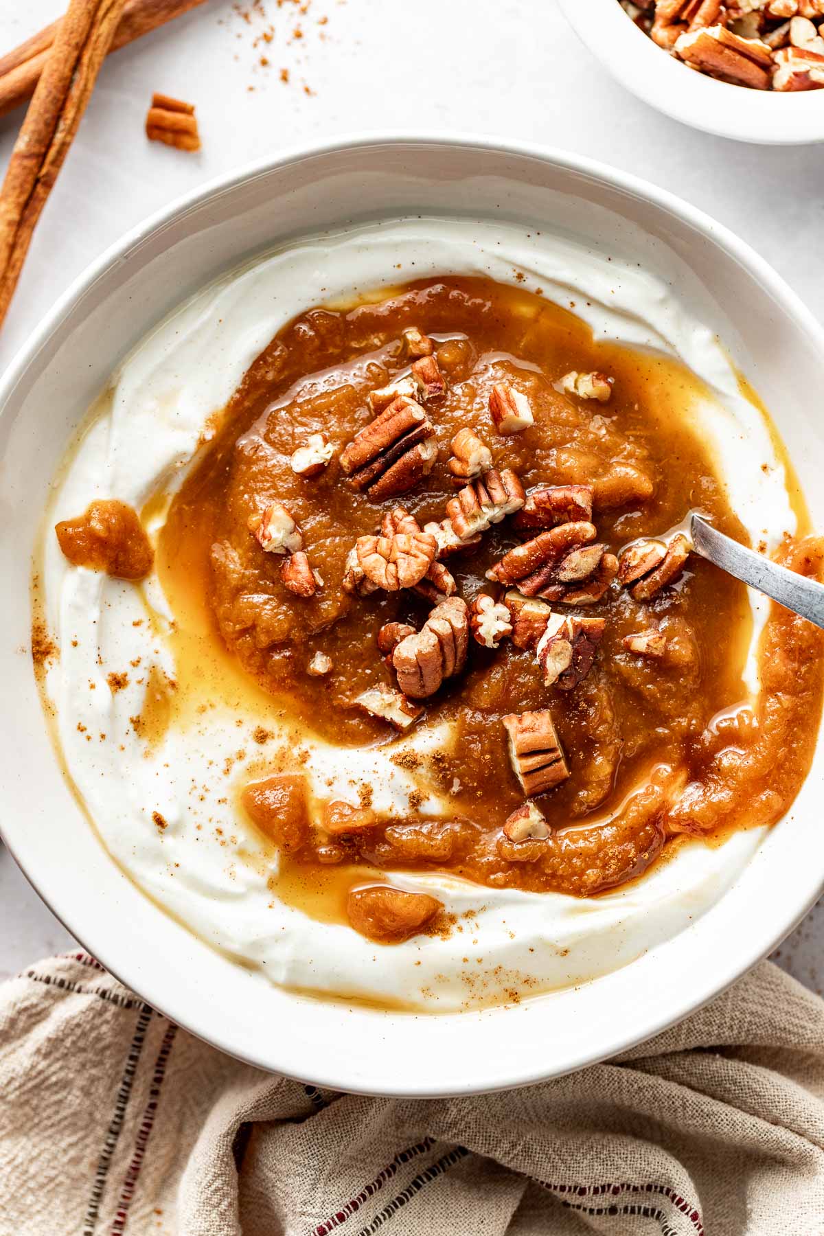 Overhead view of a bowl filled with yogurt and topped with Crockpot Pumpkin Applesauce and pieces of pecans
