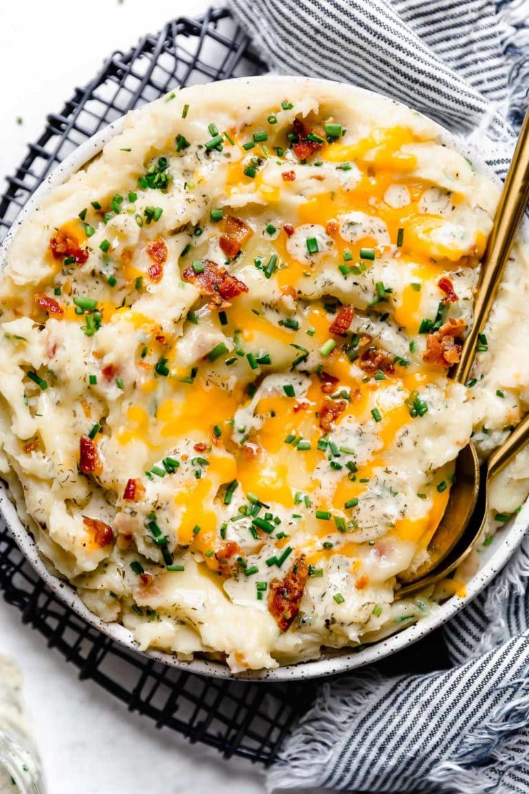 Overhead view of a bowl filled with slow cooker loaded mashed potatoes topped with melted cheese, bacon bits, and fresh herbs and seasonings. 