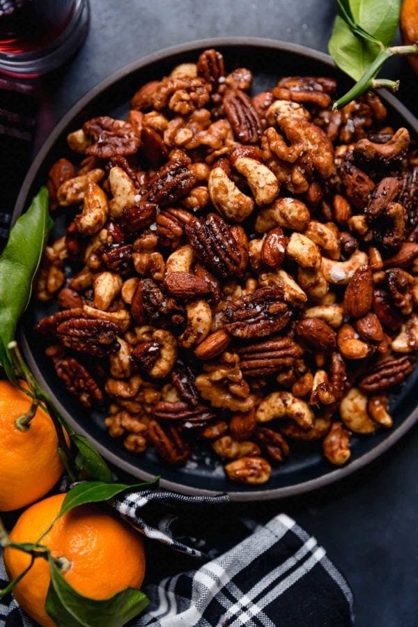 Overhead view of a black bowl on a dark grey surface filled with Slow Cooker Spiced Nuts (includes cashews, almonds, and pecans). 