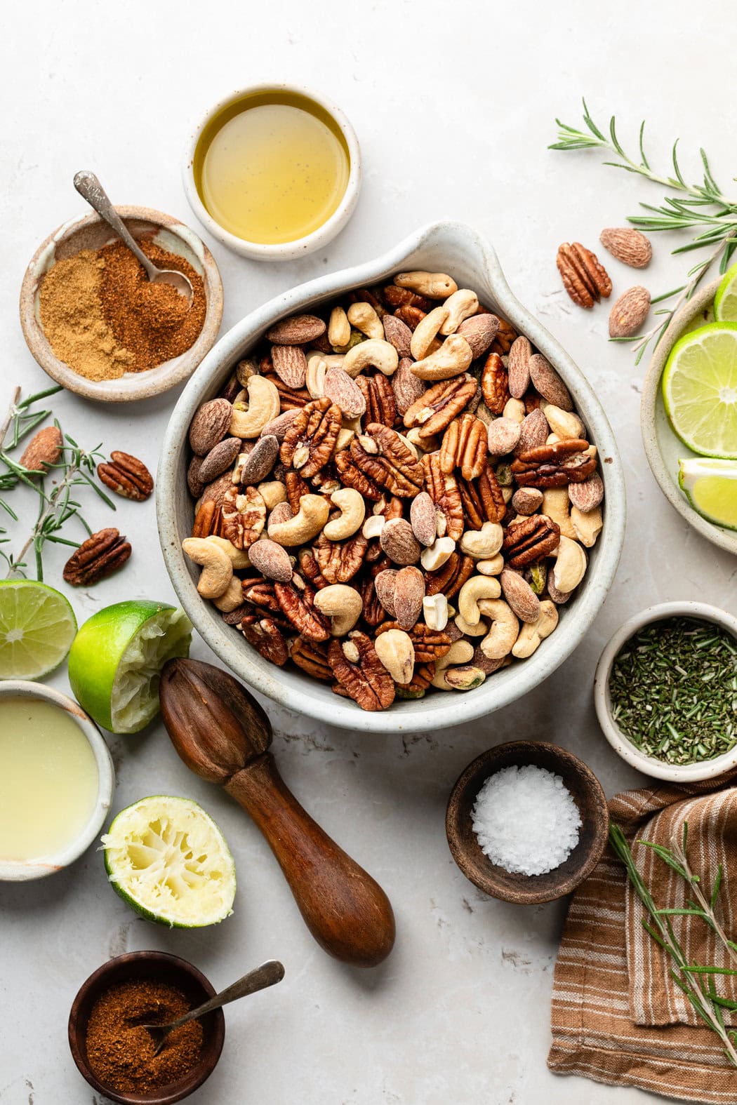 Overhead view of a variety of ingredients for Chili Rosemary Roasted Nuts in different sized bowls. 