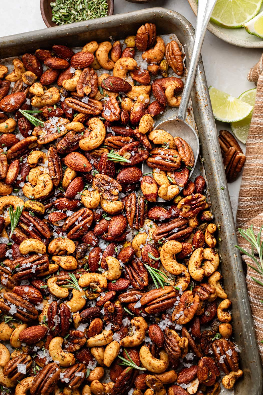 Close up view of a pan of Chili Rosemary Roasted Nuts topped with fresh rosemary and flakey sea salt. 