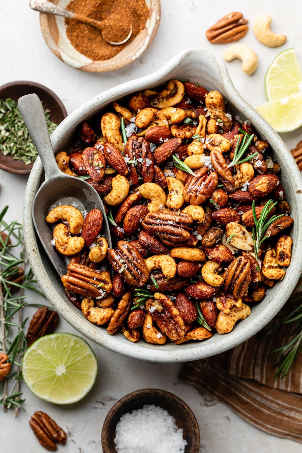 Overhead view of a bowl of freshly baked Chili Rosemary Roasted Nuts, topped with fresh rosemary and flakey sea salt. 