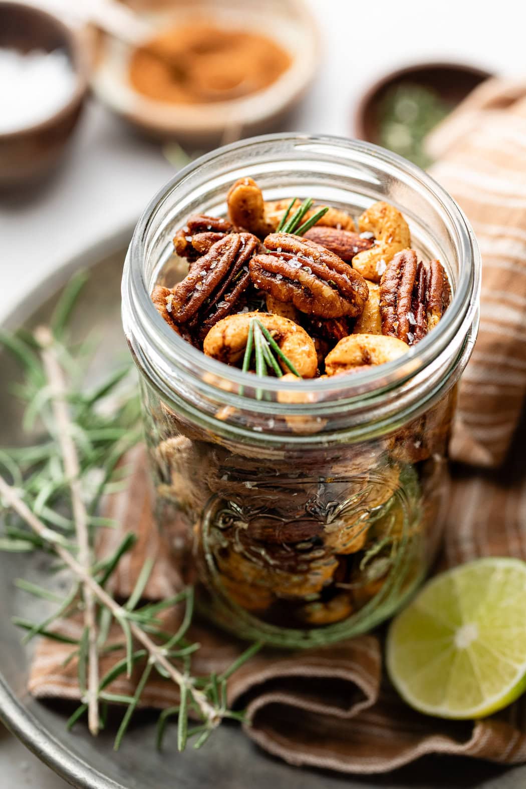 Close up view of a small mason jar filled with Chili Rosemary Roasted Nuts. 