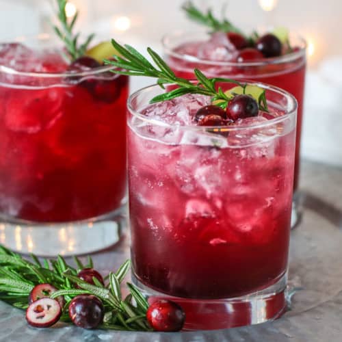 Sparkling Cranberry Kombucha Mocktail in three old-fashioned glasses and garnished with cranberries, ginger, and a rosemary sprig.