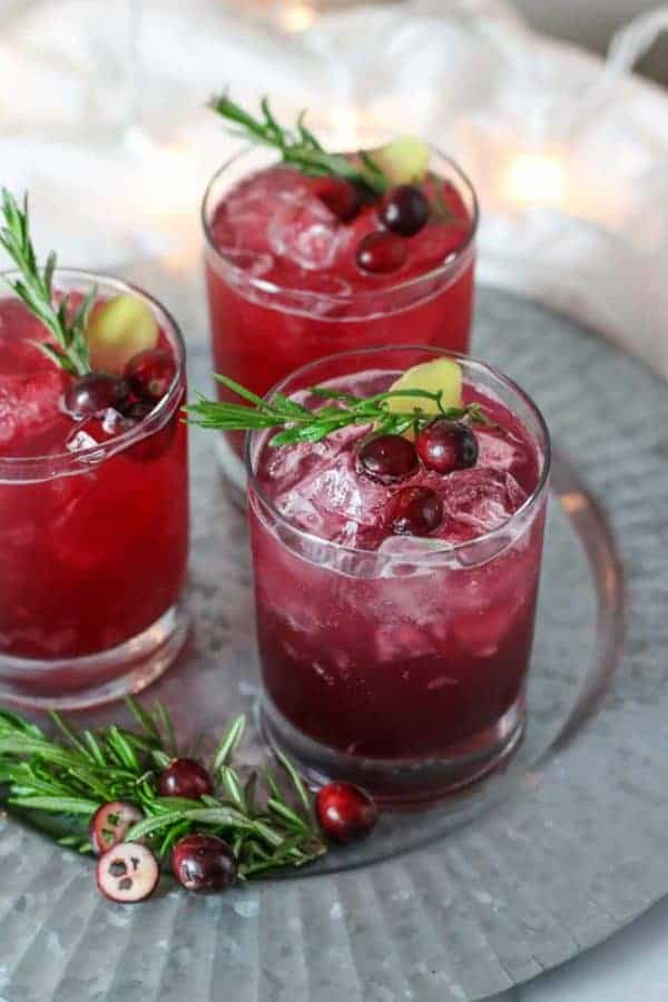 Three clear drink glasses filled with sparkling cranberry kombucha mocktail and garnished with fresh cranberries and rosemary sprigs.