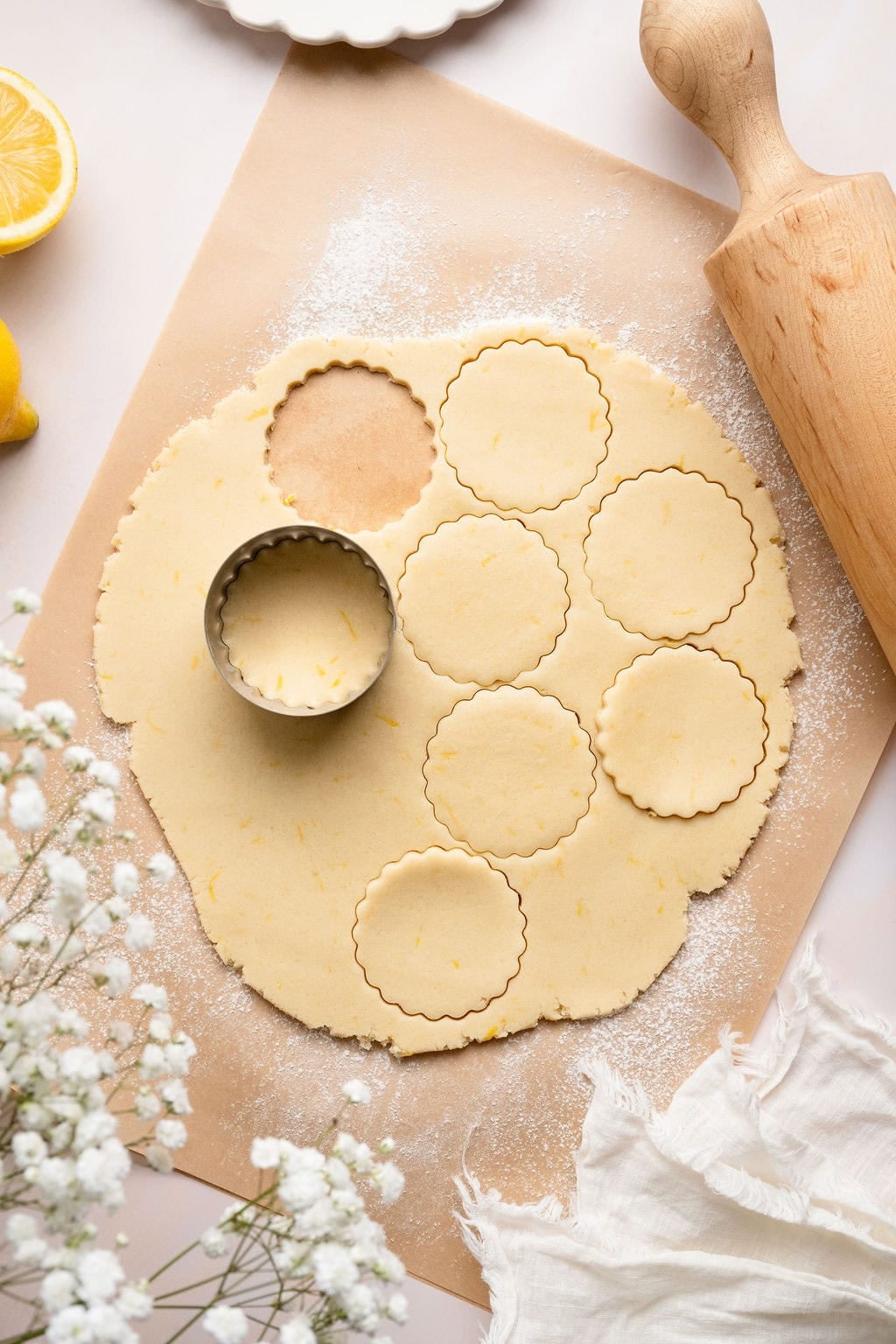 Overhead view of a large piece of lemon cookie dough rolled out on a floured piece of parchment paper with a cookie cutter on top. 