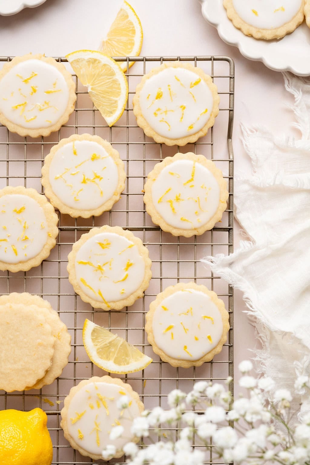 Overhead view of a cooling rack filled with frosted lemon cookies sprinkled with lemon zest. 