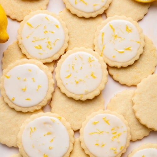 Overhead view of a variety of lemon cookies arranged on a white countertop sprinkled with lemon zest.