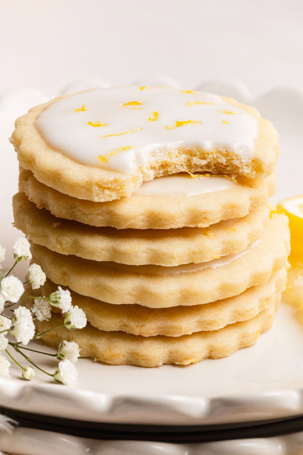 Close up view of a stack of frosted lemon cookies with the top cookie showing a bite out of it. 