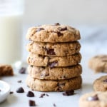 Five chocolate chip cookies stacked on top of each other with a glass of milk in the background.