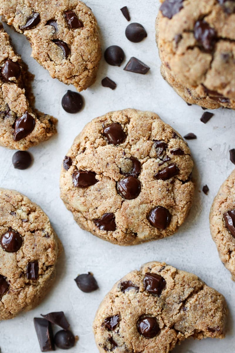 Several Paleo Chocolate Chip Cookies on a white platter with chocolate chunks and chips scattered about.