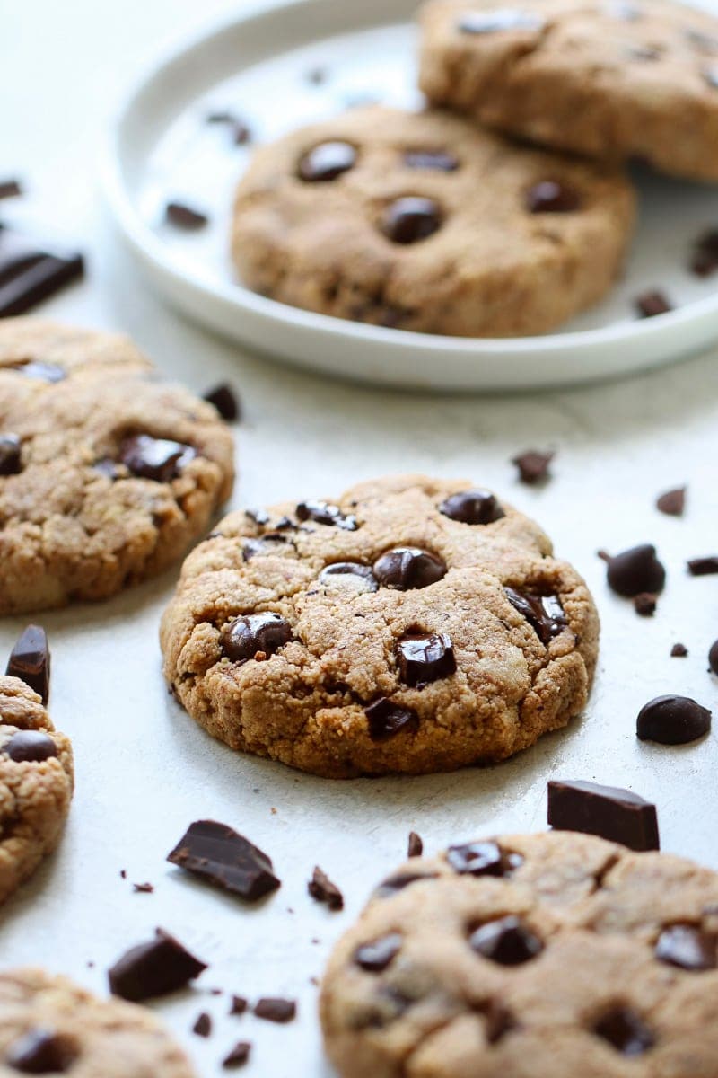 Several Paleo Chocolate Chip Cookies on a white platter with chocolate chunks and chips scattered about.