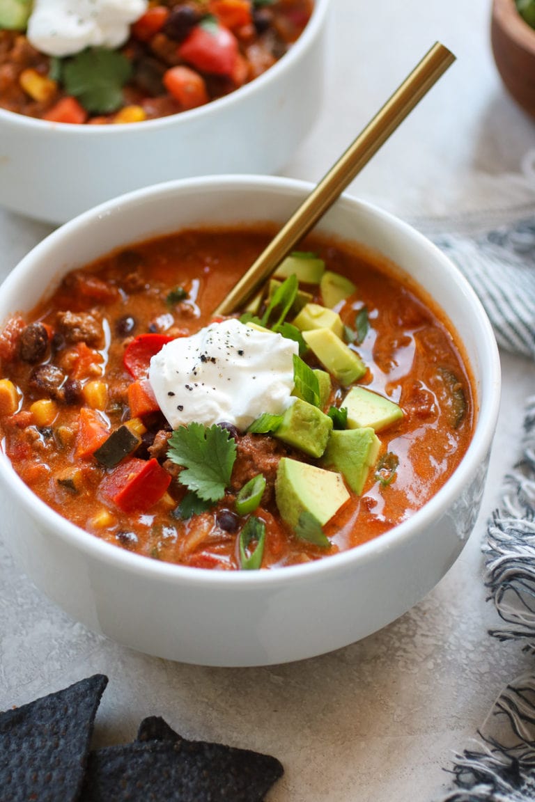 A bowl filled with taco soup topped with diced avocado and sour cream.