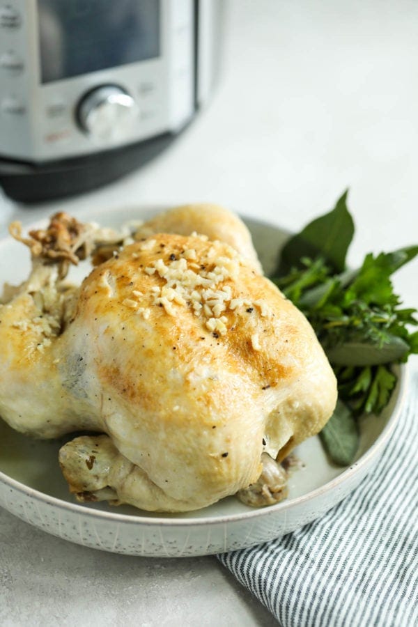 A whole chicken in a glass bowl with fresh herbs. There is an Instant Pot in the background. 